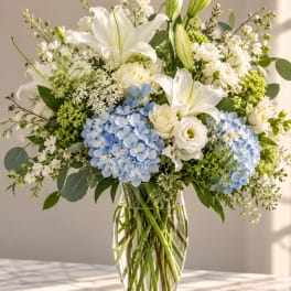 White lilies and roses with blue hydrangeas in a clear glass vase