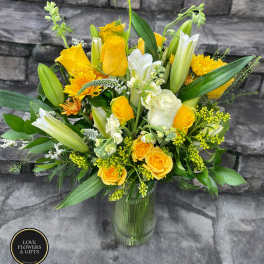 Tall yellow and white arrangement with roses and lilies in a clear glass vase