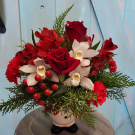 Red roses and white orchids arranged in a small vase with greenery and berries