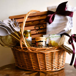 Gift basket with kitchen towels, utensils, and food items in a wicker basket