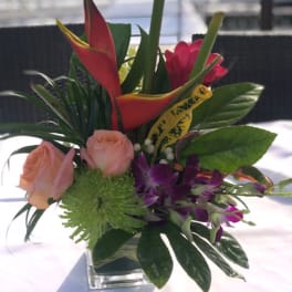 Tropical flower arrangement with roses, orchids, and calla lilies in a glass vase