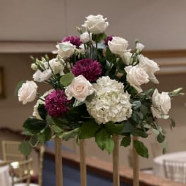 White roses and purple mums arranged in a tall centerpiece