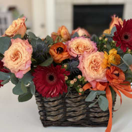 Basket arrangement of peach roses and red gerbera daisies