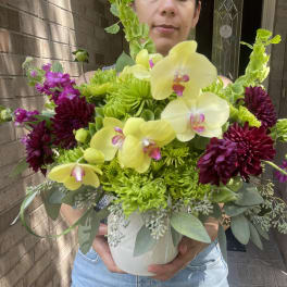 Bouquet of yellow orchids and dark purple flowers in a white vase
