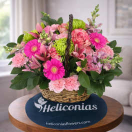 Basket arrangement of pink and green flowers with a woven handle