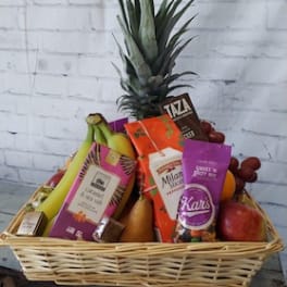 Fruit basket with a pineapple, bananas, grapes, and assorted packaged snacks