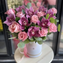 Pink roses and purple orchids arranged in a white hatbox