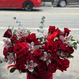 Red roses and pale orchids arranged in a red hat box