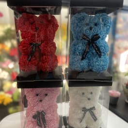 Four rose teddy bears in clear display boxes, in red, blue, pink, and white.
