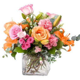 Mixed bouquet of pink and orange flowers in a clear glass vase