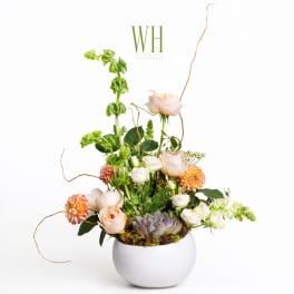 Tall floral arrangement in a white round vase with peach and white blooms