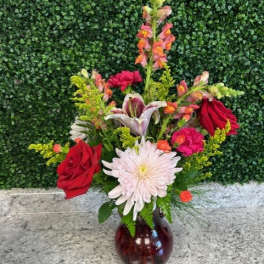 Mixed bouquet with red roses, a white daisy, and lilies in a glass vase