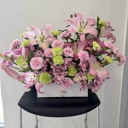 Pink lilies and carnations arranged in a white box