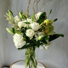 Tall arrangement of white roses, lilies, hydrangeas, and green orchids in a clear glass vase
