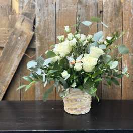 White roses in a woven basket vase with eucalyptus greenery