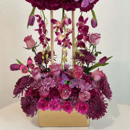 Magenta floral arrangement with tulips, roses, and butterflies in a gold vase
