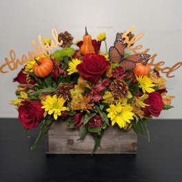 Fall floral arrangement with roses, daisies, pumpkins, and butterflies in a wooden box