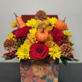 Bouquet of red roses and yellow daisies in a floral box with small pumpkins