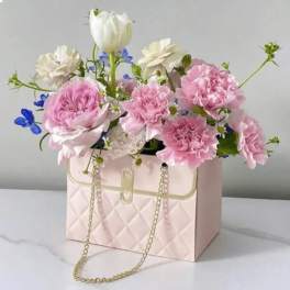 Pink and white flowers arranged in a quilted handbag-shaped box with a chain strap.