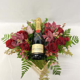 Red roses and pink orchids arranged around a champagne bottle