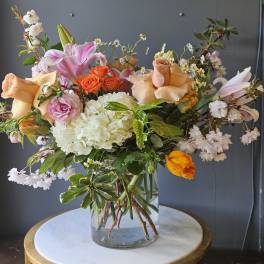 Mixed arrangement of peach roses, pink lilies, and white hydrangeas in a clear glass vase