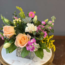 Peach roses and pink flowers in a square glass vase