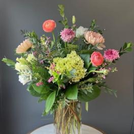 Mixed bouquet of pink, peach, and white flowers in a clear glass vase