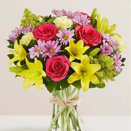 Bouquet of pink roses, yellow lilies, and lavender daisies in a glass vase