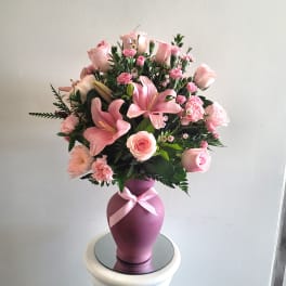 Pink floral arrangement in a purple vase with a ribbon