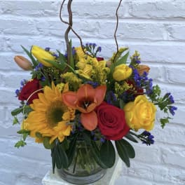 Colorful mixed flower arrangement in a glass vase with a bird ornament