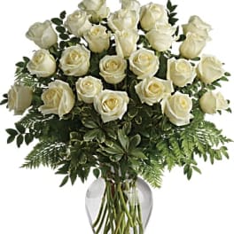 White roses arranged in a clear glass vase with greenery