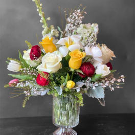 Mixed bouquet of roses, tulips, and white blooms in a clear glass vase
