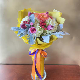 Bouquet of pink and white flowers in a clear glass vase with yellow wrap