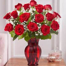 Red roses arranged in a red glass vase with baby's breath