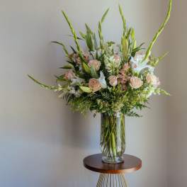 Tall bouquet of pale roses, white lilies, and greenery in a clear glass vase
