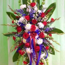 Tall standing floral spray with red roses, white daisies, and blue flowers