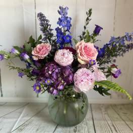 Pink roses and purple flowers arranged in a glass vase