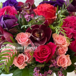 Mixed bouquet of pink, purple, and red flowers in a white vase