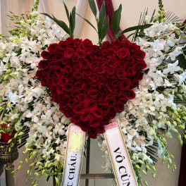 Heart-shaped red rose arrangement surrounded by white orchids on an easel