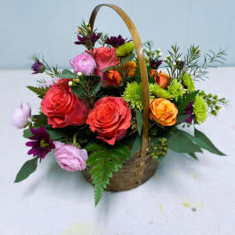 Basket of mixed roses and daisies in pink, coral, orange, and green