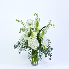 White floral arrangement in a clear glass vase with tall green accents