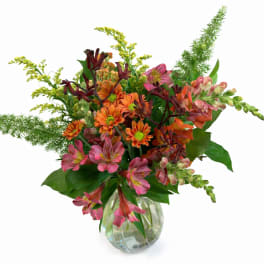 Mixed pink, orange, and burgundy flowers in a clear glass vase