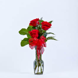 Three red roses in a clear glass vase with a red ribbon