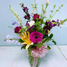 Mixed bouquet in a glass vase with pink ribbon and bright gerbera, lilies, and snapdragons