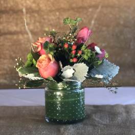 Pink roses in a green glass jar with berries and foliage