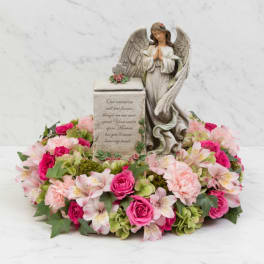 Angel figurine surrounded by pink flowers in a memorial wreath