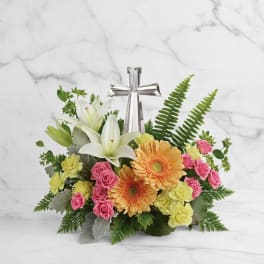 Floral arrangement with white lilies, pink roses, orange gerberas, and a silver cross