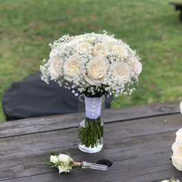 Cream rose bouquet in a glass vase with a matching boutonniere on a table