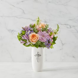 Pastel flower arrangement in a white vase with a cross emblem