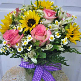 Bouquet of pink roses, sunflowers, and white daisies with a purple ribbon